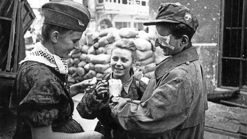 Photo credit: Joachim Joachimczyk, public domain / Warsaw Uprising: Two nurses and a wounded insurgent (on the right) from the “Parasol” battalion after exiting the canal on Warecka Street near Nowy Świat (Środmiescie-North). In the middle stands Maria Stypułkowska-Chojecka “Kama.” On the right Krzysztof Palester “Krzych”.